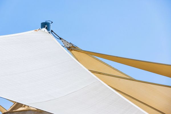 Close-up of white and beige sunshade sails against a clear blue sky.