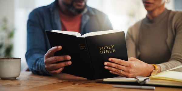 Two people reading the Holy Bible together at a wooden table.