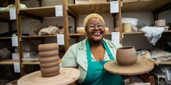 Smiling potter proudly displays two clay creations in her workshop.