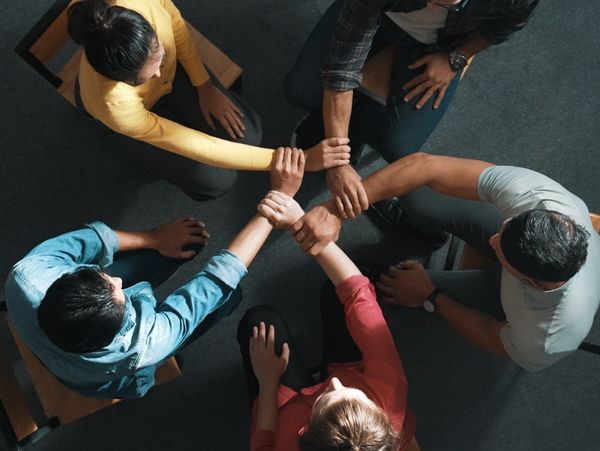 Four people sitting in a circle holding each other's wrists in unity.