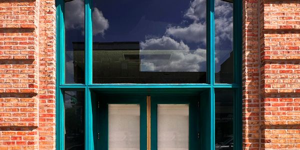 A teal-framed glass door with brick walls and cloudy sky reflection.