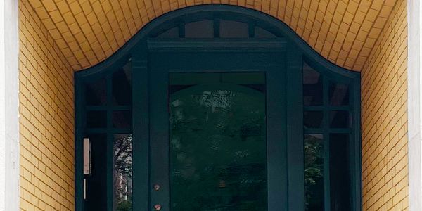 Elegant dark green door framed by yellow brick archway and white columns.