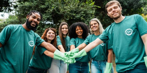 Group of volunteers in green shirts joining hands outdoors.
