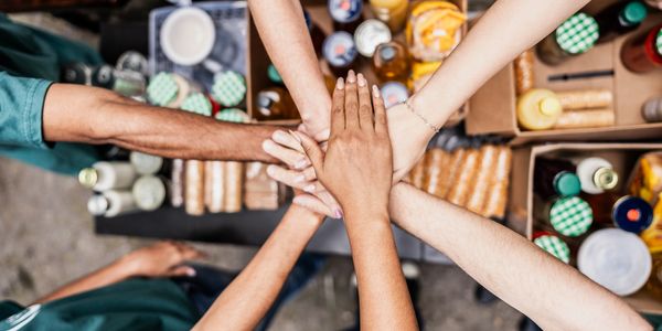 Volunteers joining hands over donated food boxes in a show of teamwork and unity.