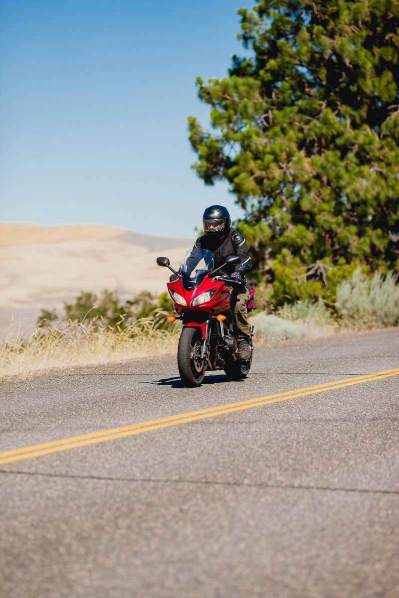 Motorcyclist riding on an open road in the hills among giant power lines and transformers. He is riding in the summer on a sunny day and showing determination and focus. He is fully suited up in safety equipment.