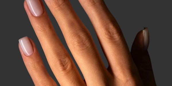 Hand with neatly manicured nails painted in a soft, translucent nude color.