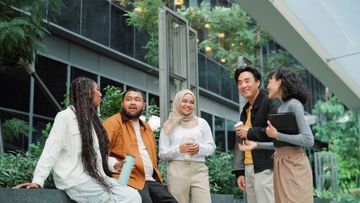 A diverse group of young professionals chatting outdoors in a modern urban setting.
