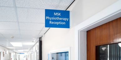 Blue projecting sign indicating MSK Physiotherapy Reception in a hospital corridor.
