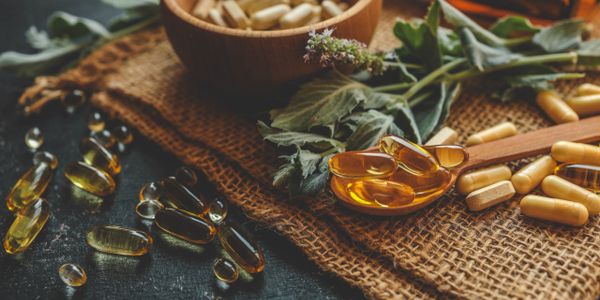 Capsules and herbal leaves on rustic fabric, highlighting natural supplements.
