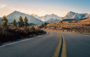 A winding road leading towards snow-capped mountains under a clear sky.