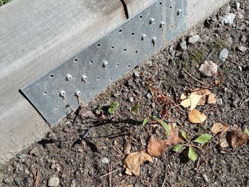 Metal bracket attached to wooden surface near soil with leaves.