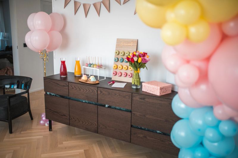 An array of colorful donuts and cake pops artfully presented on a wooden board for a baby shower, complemented by a bouquet of tulips.