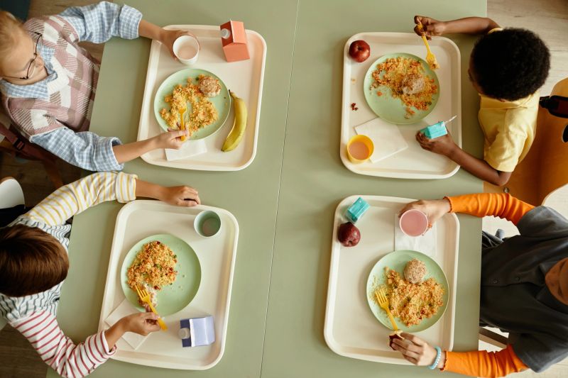 Top view of primary school children sitting together at large table enjoying eating healthy lunch in cafeteria