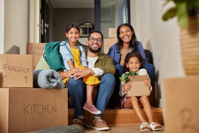 Happy family sitting on the steps surrounded by moving boxes in their new home.
