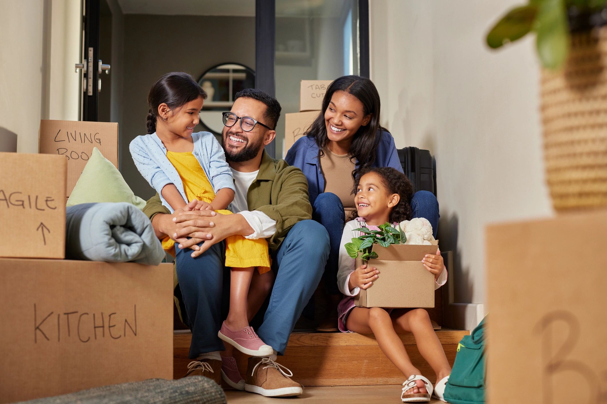 A smiling family of four takes a break on the entryway steps of their new home, surrounded by labele