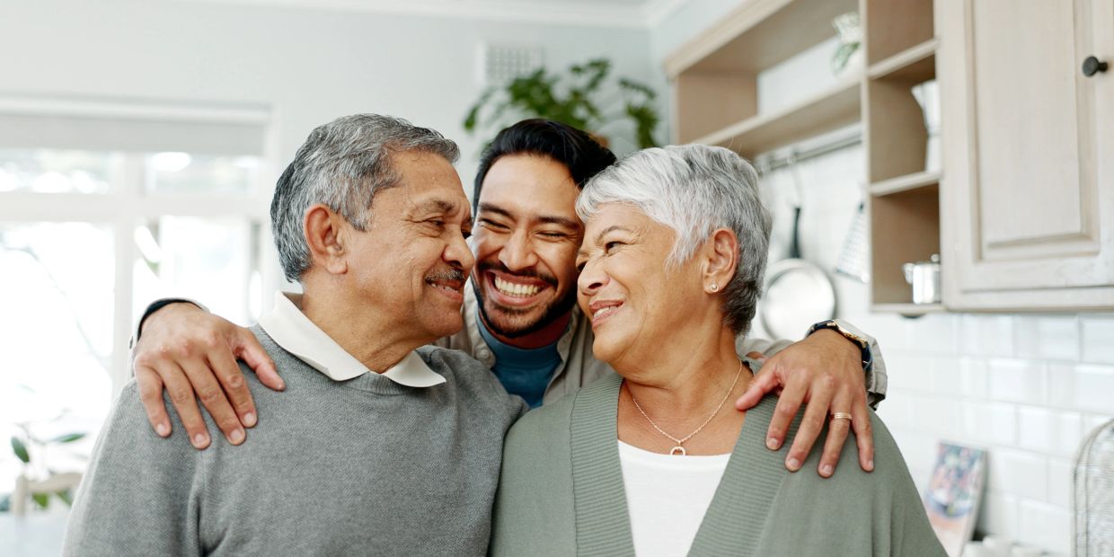 Happy young man hugging his elderly parents in a warm kitchen setting.