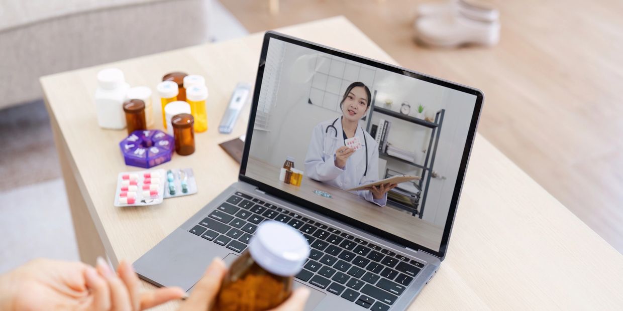 Person consulting a doctor online with medication on table.