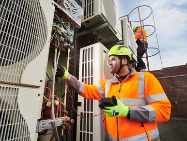 Technicians in safety gear inspecting and repairing HVAC units outdoors.