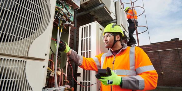 Technicians in safety gear inspecting and repairing HVAC units outdoors.