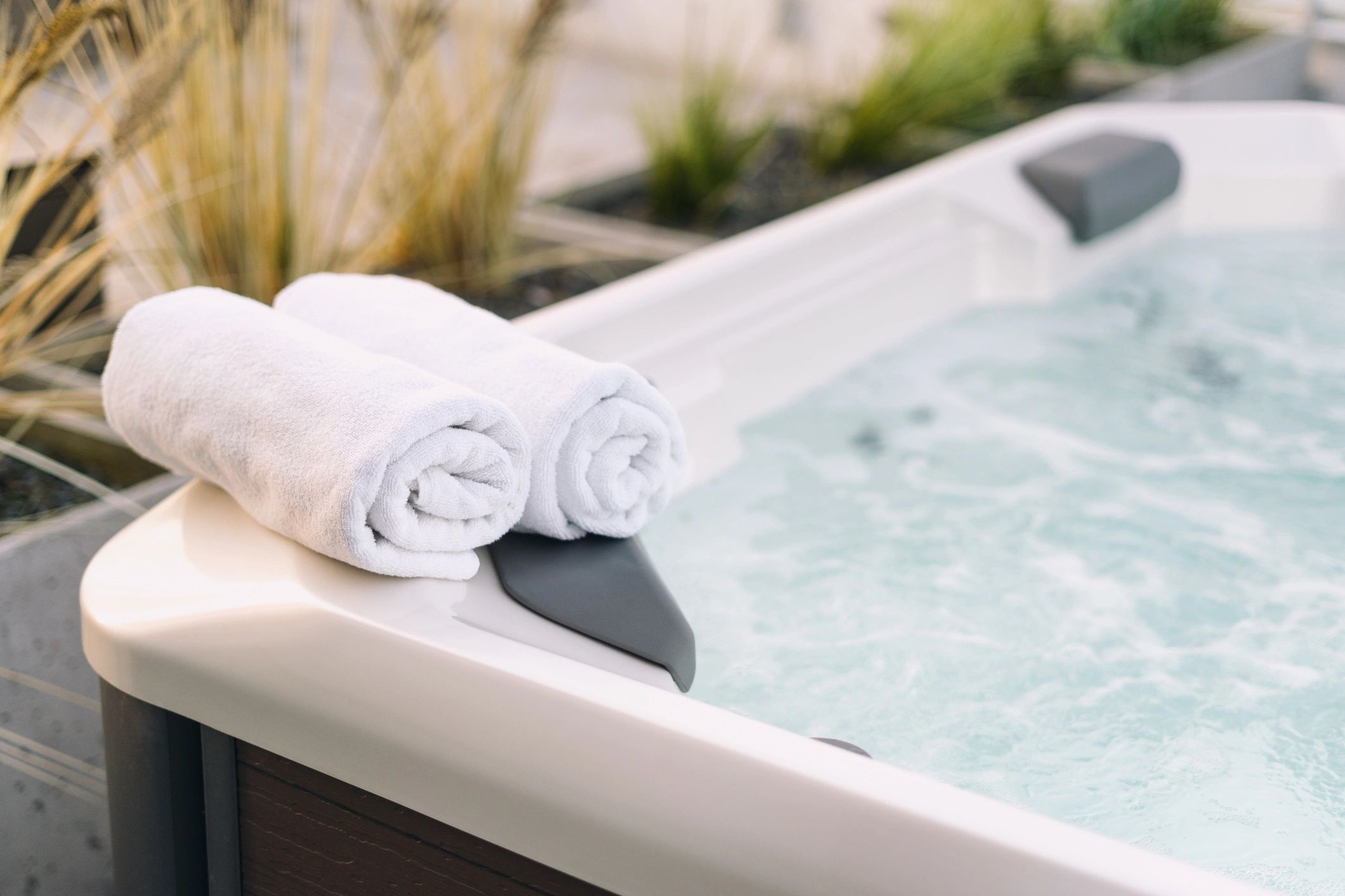 Two rolled white towels on the edge of a bubbling hot tub.
