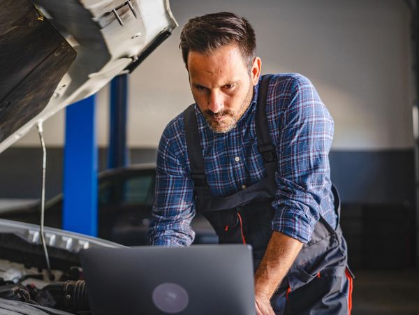 Mechanic using a laptop to diagnose a car with its hood open.