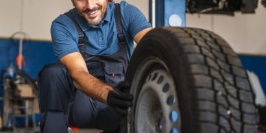 Mechanic inspecting a car tire in a workshop, smiling.