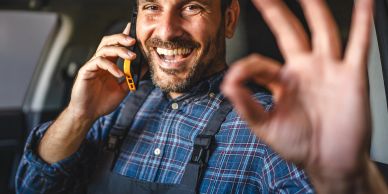 Man smiling and making OK sign while talking on phone.