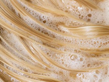 Blonde hair strands covered in soapy foam during washing.