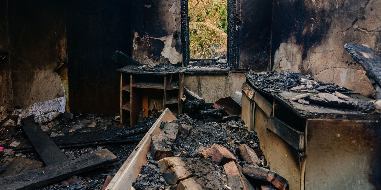Room heavily damaged by fire with charred furniture and debris.