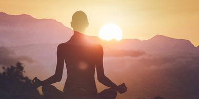 silhouette of person meditating with mountains in background