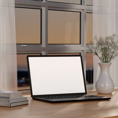 Minimalist workspace with laptop, books, and vase by a window at sunset.