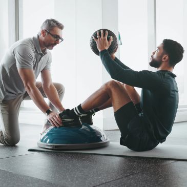 Trainer assisting man with medicine ball exercise.