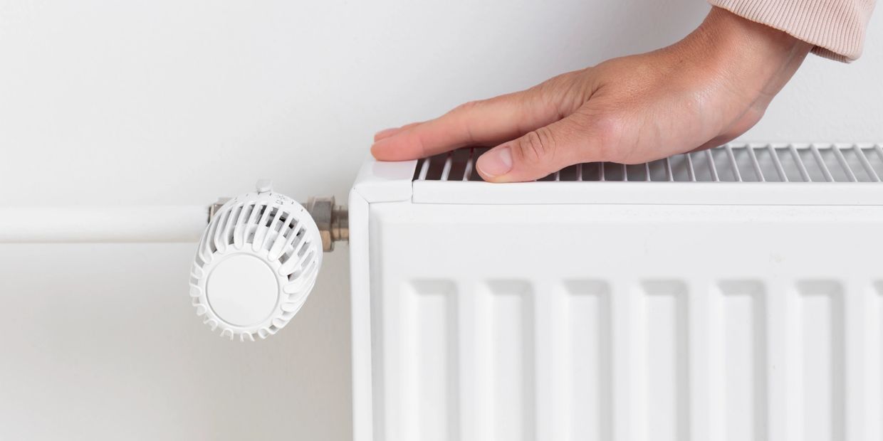Hand touching a white radiator thermostat in a minimalistic room.