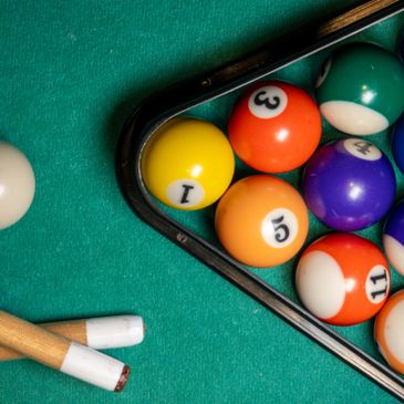 Billiard balls arranged in a triangle with two pool cues on a green felt table.