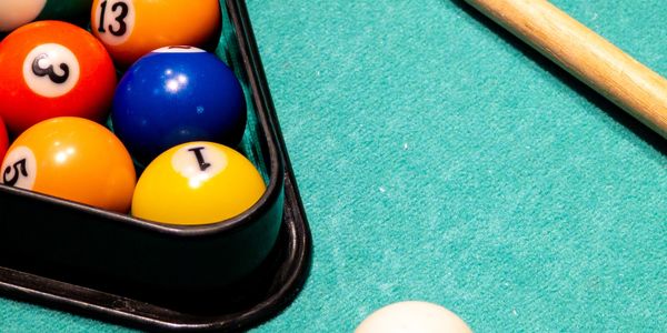 Pool balls arranged in a triangle with a cue and white ball on a green felt table.