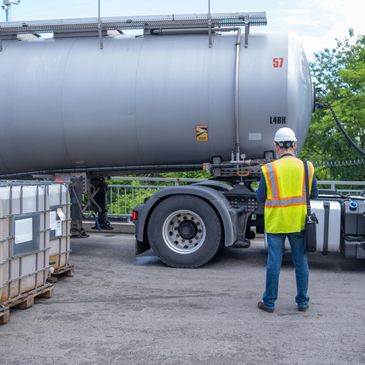 Worker inspecting a large tanker truck at an industrial site.