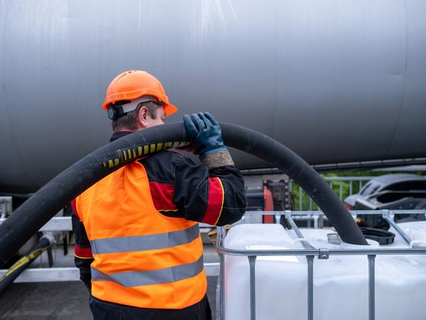 Worker in safety gear handling a large hose at an industrial site.