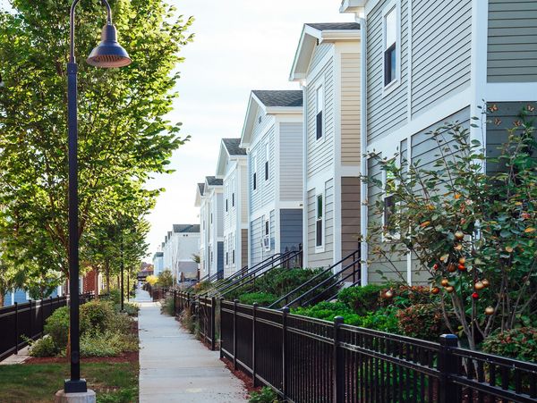 Row of modern townhouses along a tree-lined sidewalk with black iron fencing.