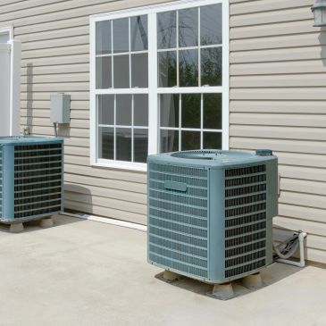 Two outdoor air conditioning units next to a beige house.