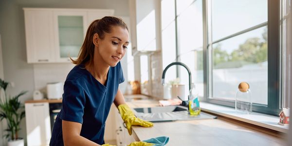 Woman cleaning kitchen counter wearing yellow gloves.