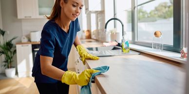 Woman cleaning kitchen countertop with gloves and cloth.