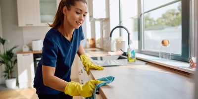 Woman cleaning kitchen countertop with yellow gloves.
