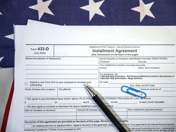IRS Form 433-D with American flag, pen, and paperclip.