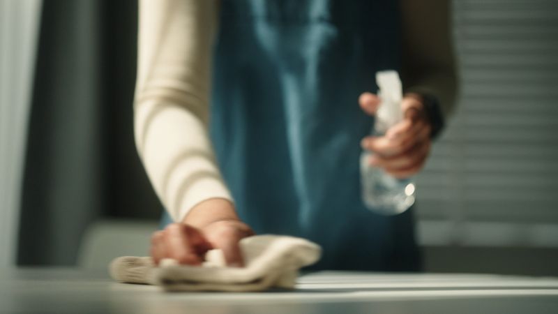 Close-up hand of woman spray cleaner and wiping the table.