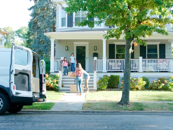 Family unloading boxes from a van in front of a house.