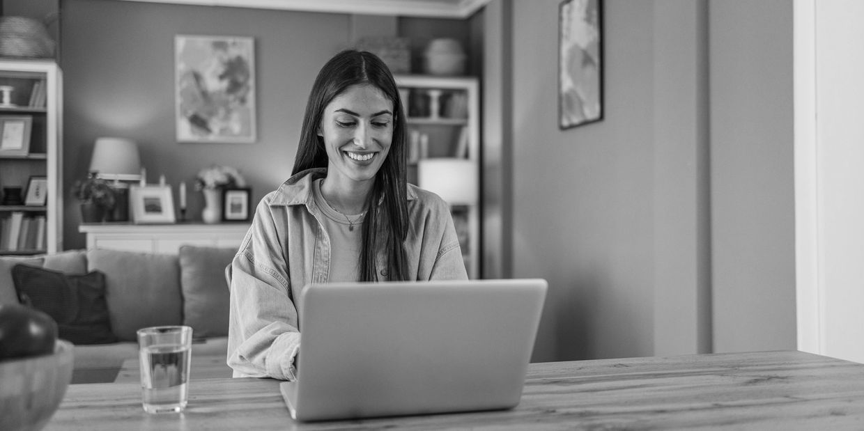 Smiling woman working on a laptop at a wooden table.