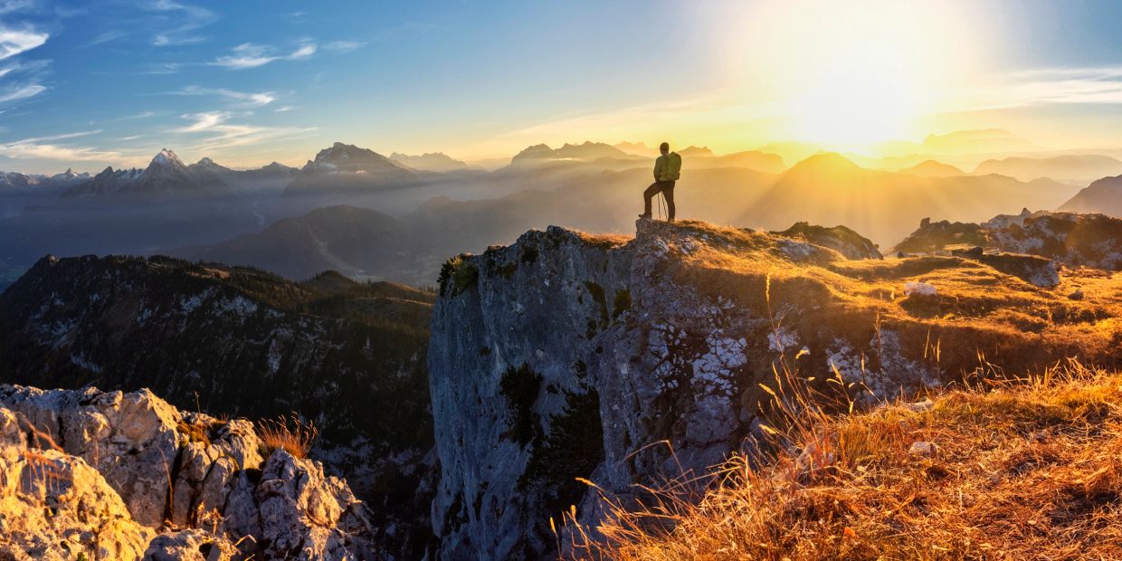 Person standing on a mountain cliff at sunrise.