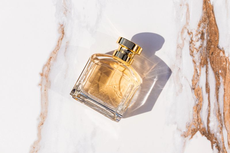 A chic bottle with a gold cap of cosmetic perfume on an abstract marble background. top view. Product presentation. a blank bottle mockup. sunlight