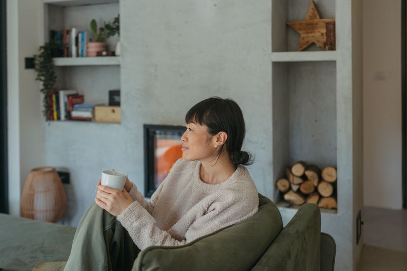 Photo of a woman relaxing in her living room, drinking a cup of warm coffee,  as she enjoys a moment of tranquility.