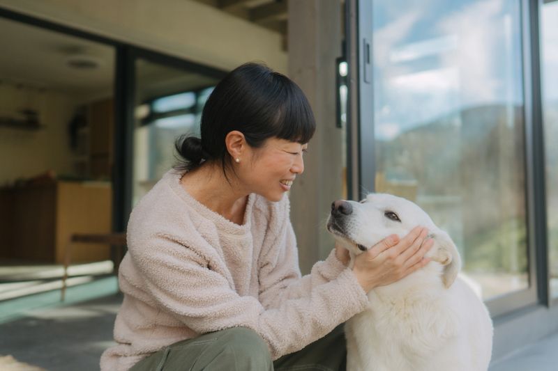Photo of a woman petting her dog and enjoying her afternoon outside a remote house.